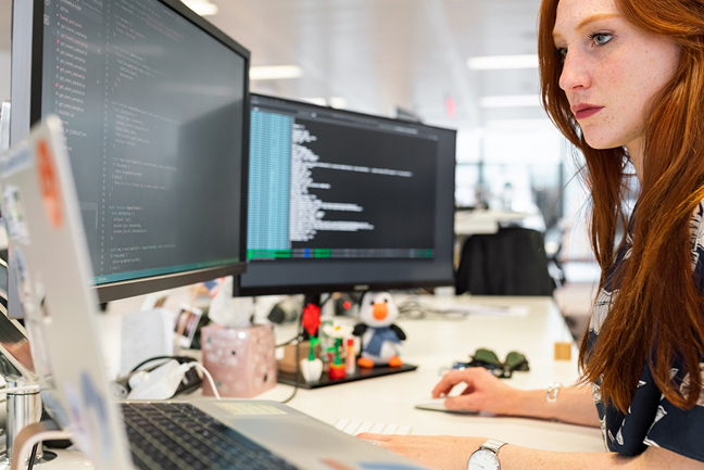 Red head woman looking at dual monitors