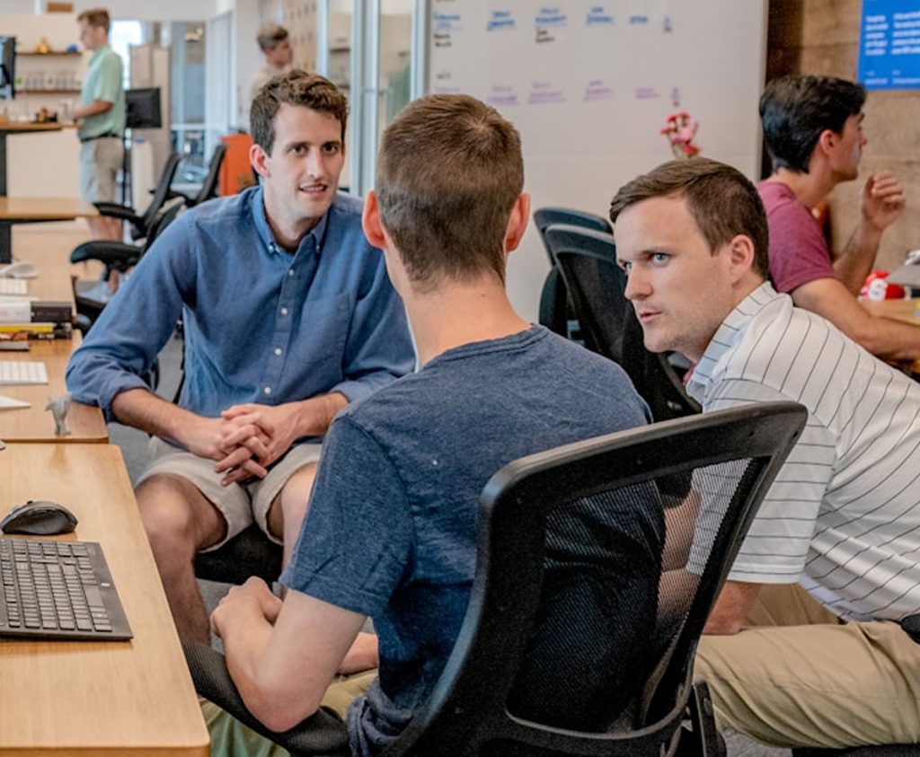 Three men sitting in front of laptop talking